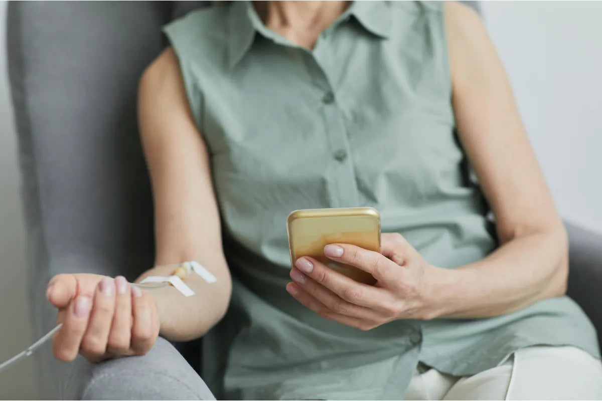 Woman seated with an IV drip cannula taped to her arm during a vitamin drip session